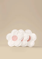 Le Lolo flower-shaped disposable nursing pad with pink centers on a beige background