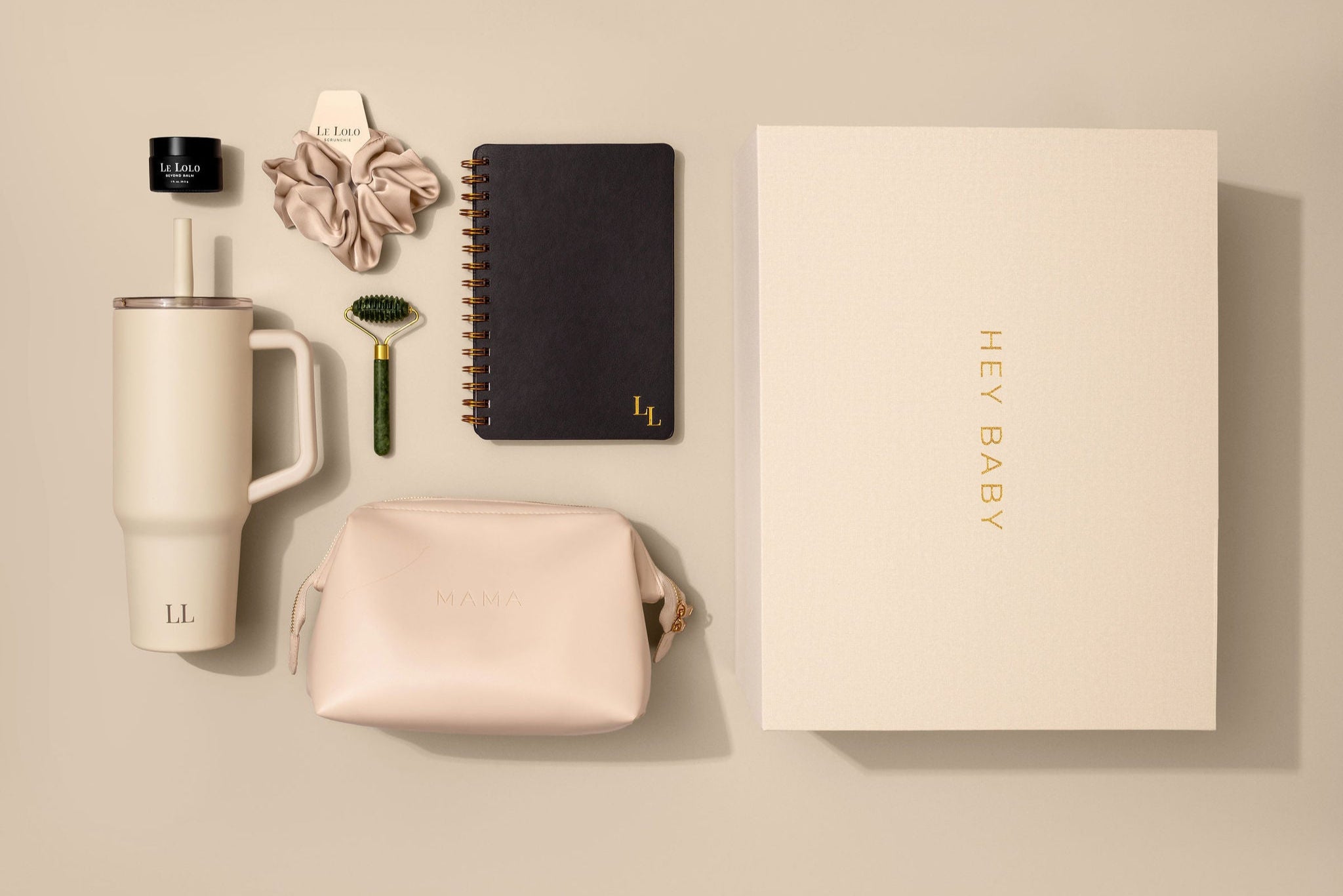 The Every Mama Set by Le Lolo is a collection of items including a 40oz tumbler, satin scrunchie, journal with JOURNAL PROMPTS FOR MAMA + DAILY TRACKER FOR BABY, pure green jade facial roller, 100% organic Beyond Balm, and vegan leather mama carrying bag, packed in a linen memory keepsake box on a beige background